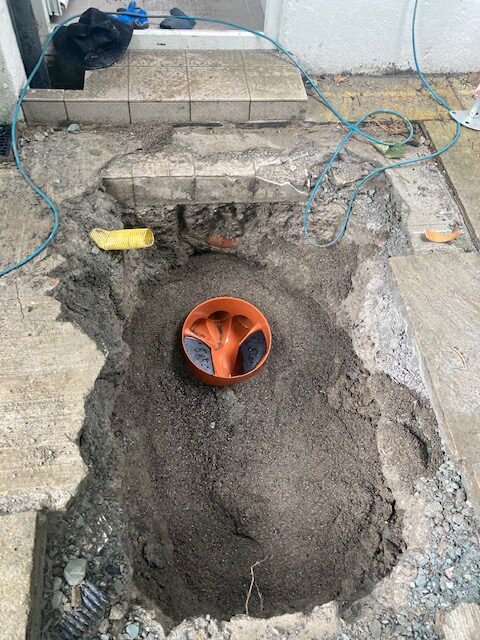 Excavated area showing a newly installed underground drain pipe access point surrounded by soil