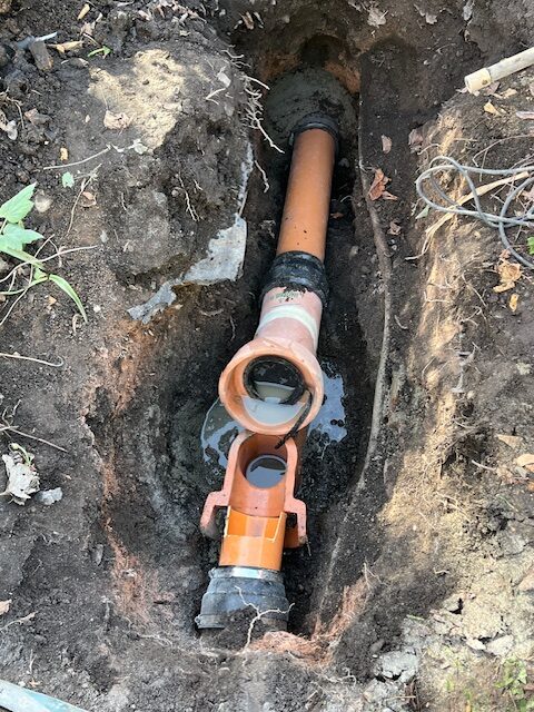 Excavated section of a damaged underground drain pipe being repaired with new fittings and connectors