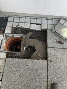 Partially excavated outdoor drain access point with surrounding paving removed for inspection and repair